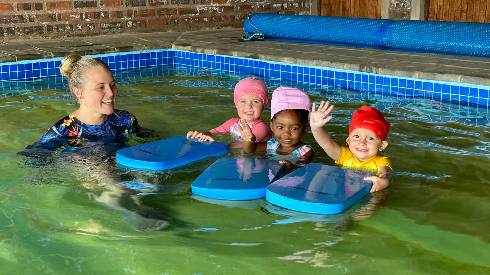 Instructor and three little swimmers smiling with kickboards in the warm pool